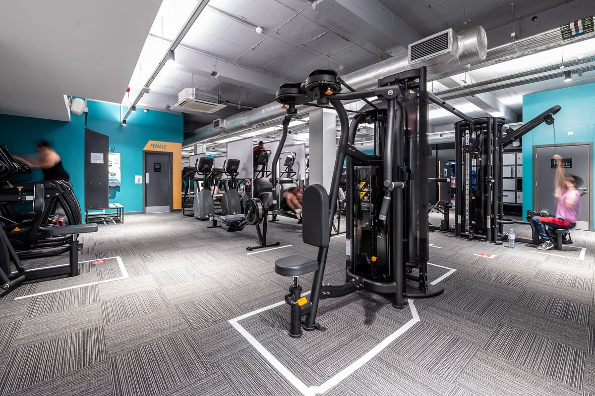 PureGym London Sydenham: Gym with weight machines, free weights, pads, and mirrored walls in teal and grey color scheme.