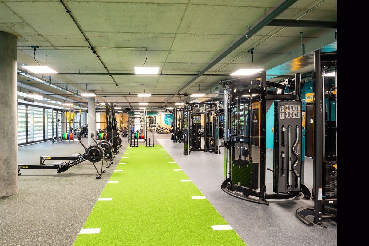 PureGym Genf Le Bouchet: Gym with resistance machines, free weights, benches, green turf area, and mirrored walls.
