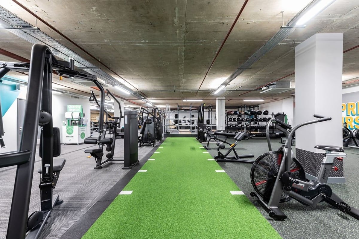 PureGym London Angel: Rows of weight machines, cable stations, green turf area, concrete interior design.