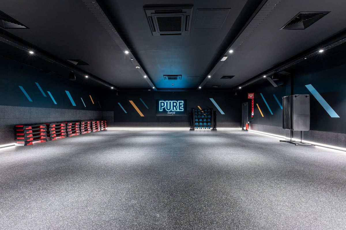 PureGym Glasgow Giffnock: Rows of red resistance bands, mirrors along walls, and blue Pure branding sign in dimly-lit space.