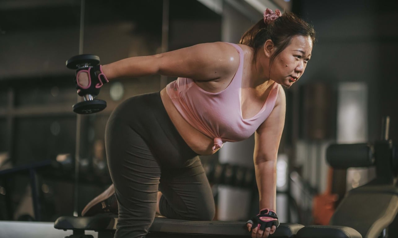 Woman lifting dumbbell in gym wearing pink top and black leggings