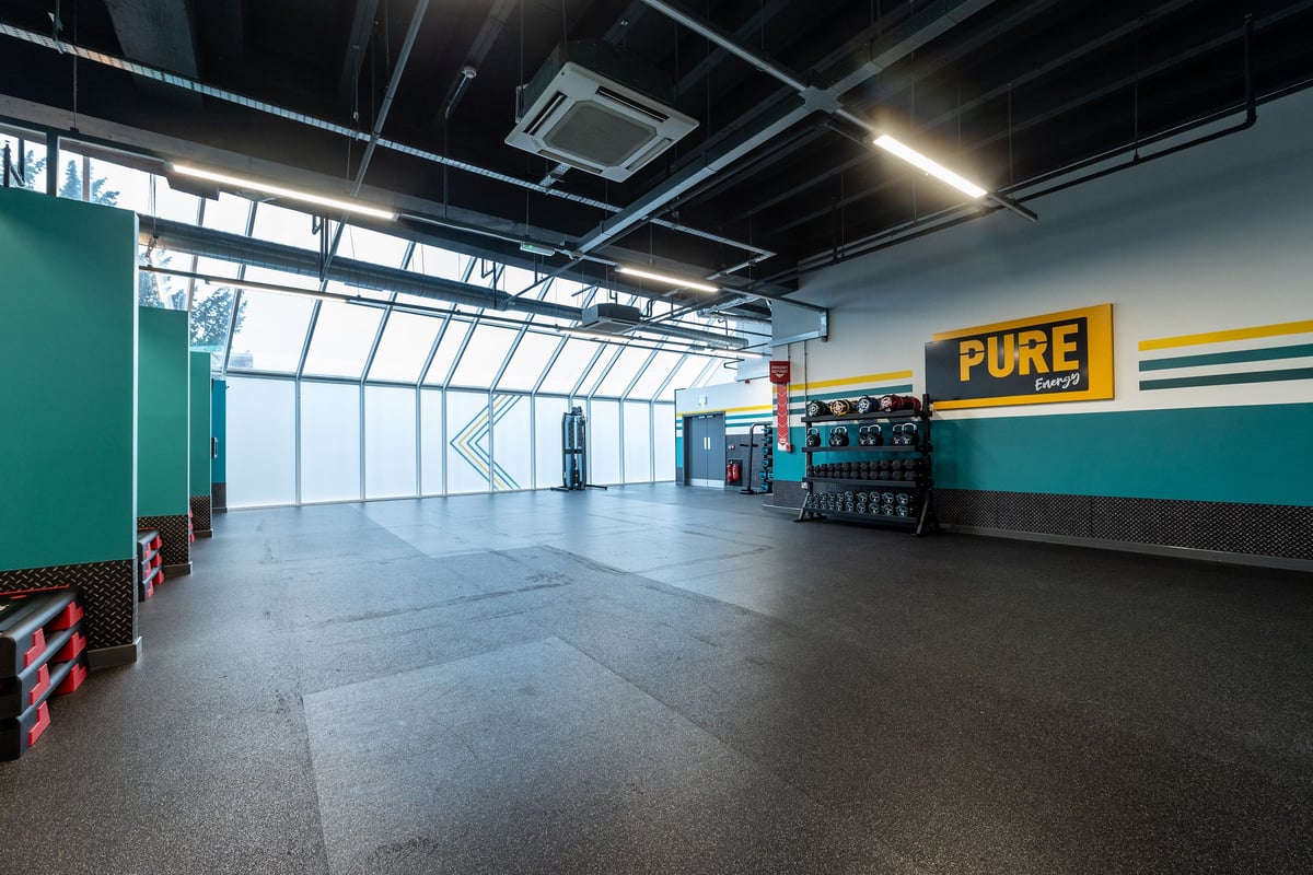 PureGym Ipswich Buttermarket: Resistance training area with free weights, rubberized flooring, teal walls, and mirror.