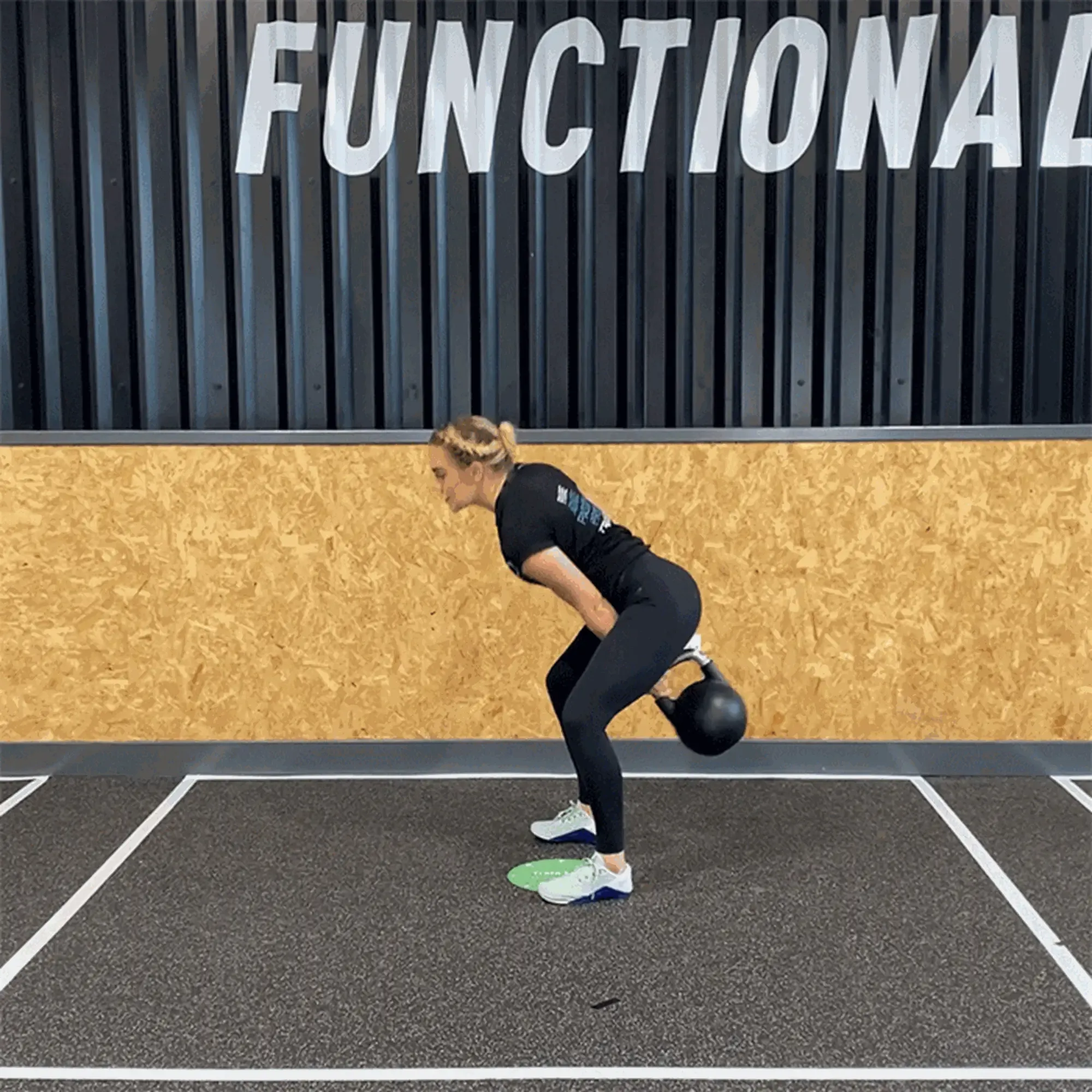 Woman performing kettlebell swing exercise in gym with FUNCTIONAL sign on wall