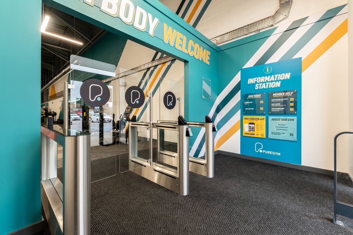 PureGym Sheffield Meadowhall Retail Park: Welcome area with turnstiles, information display, and company branding.