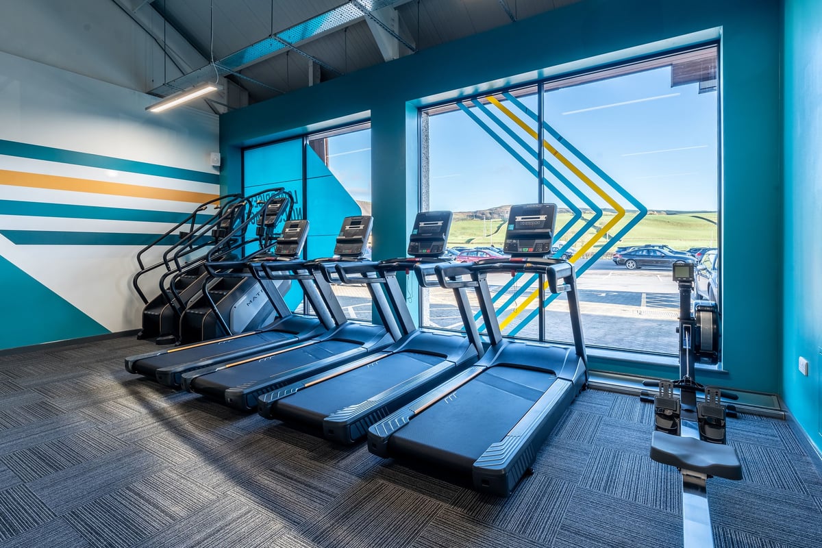 PureGym Kendal: Rows of treadmills facing floor-to-ceiling windows with colourful wall designs.