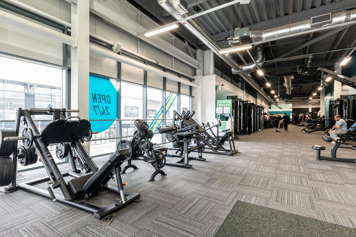 PureGym Chatham: Weight machines, leg presses, benches, and exposed piping on the ceiling in a gym setting.