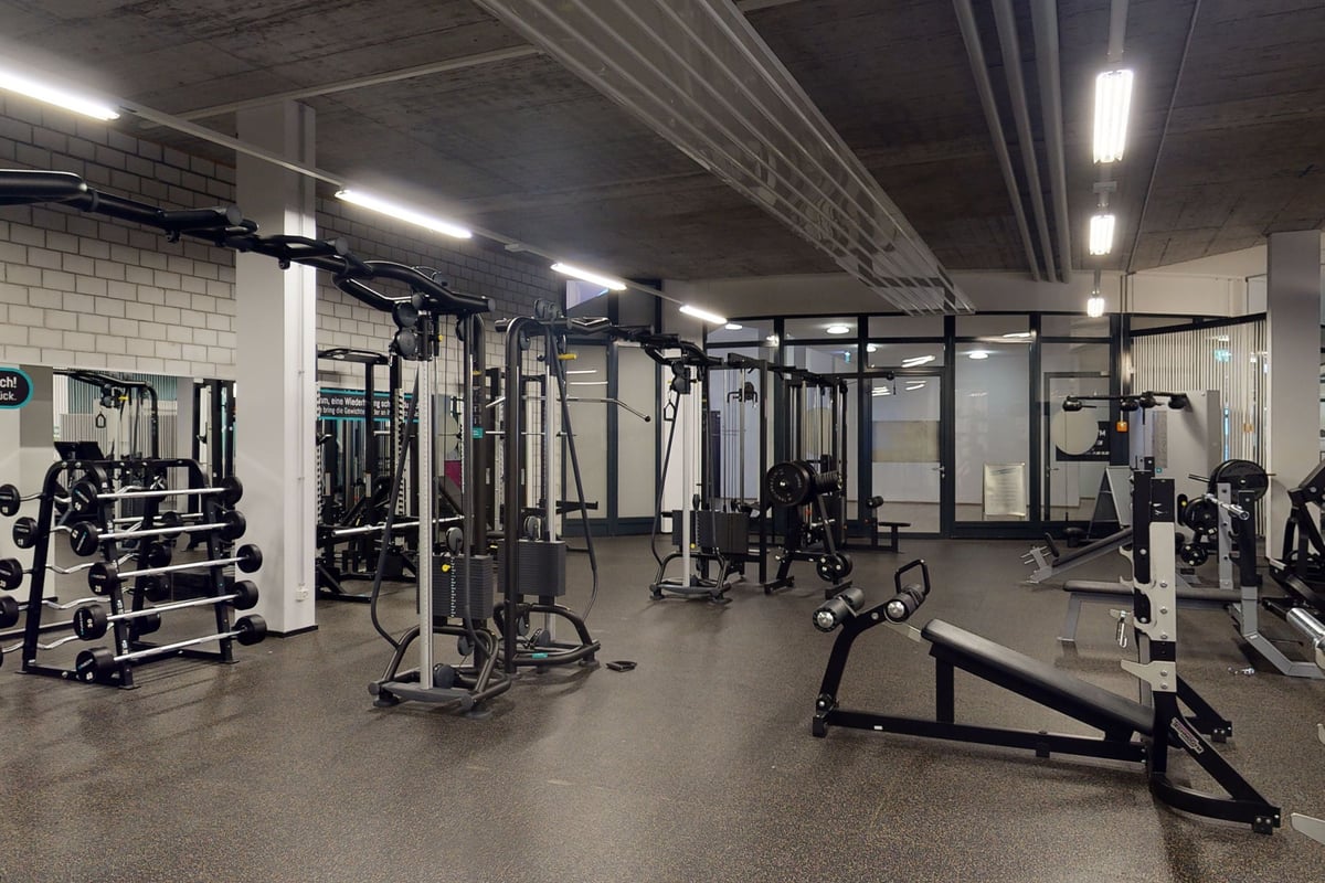 PureGym Chur: Fitnessstudio mit Kabelgeräten, Hockenständern, Bänken, Freihanteln, gummiertem Boden und freiliegenden Deckenrohren.
