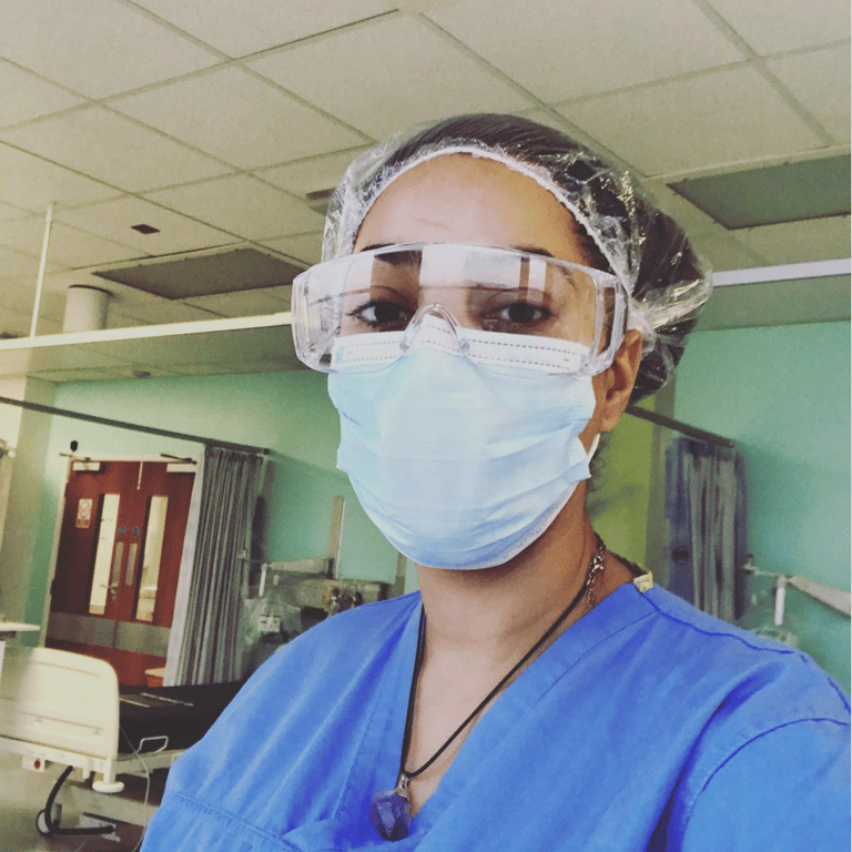 Healthcare worker wearing protective glasses, face mask, hairnet, and blue scrubs
