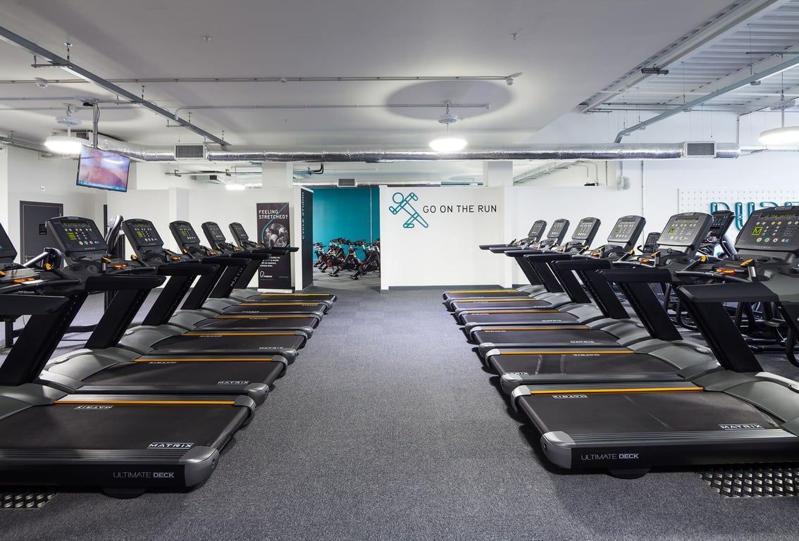 PureGym East Kilbride: Rows of treadmills, wall mural promoting 'On The Run', industrial ceiling with lighting fixtures.