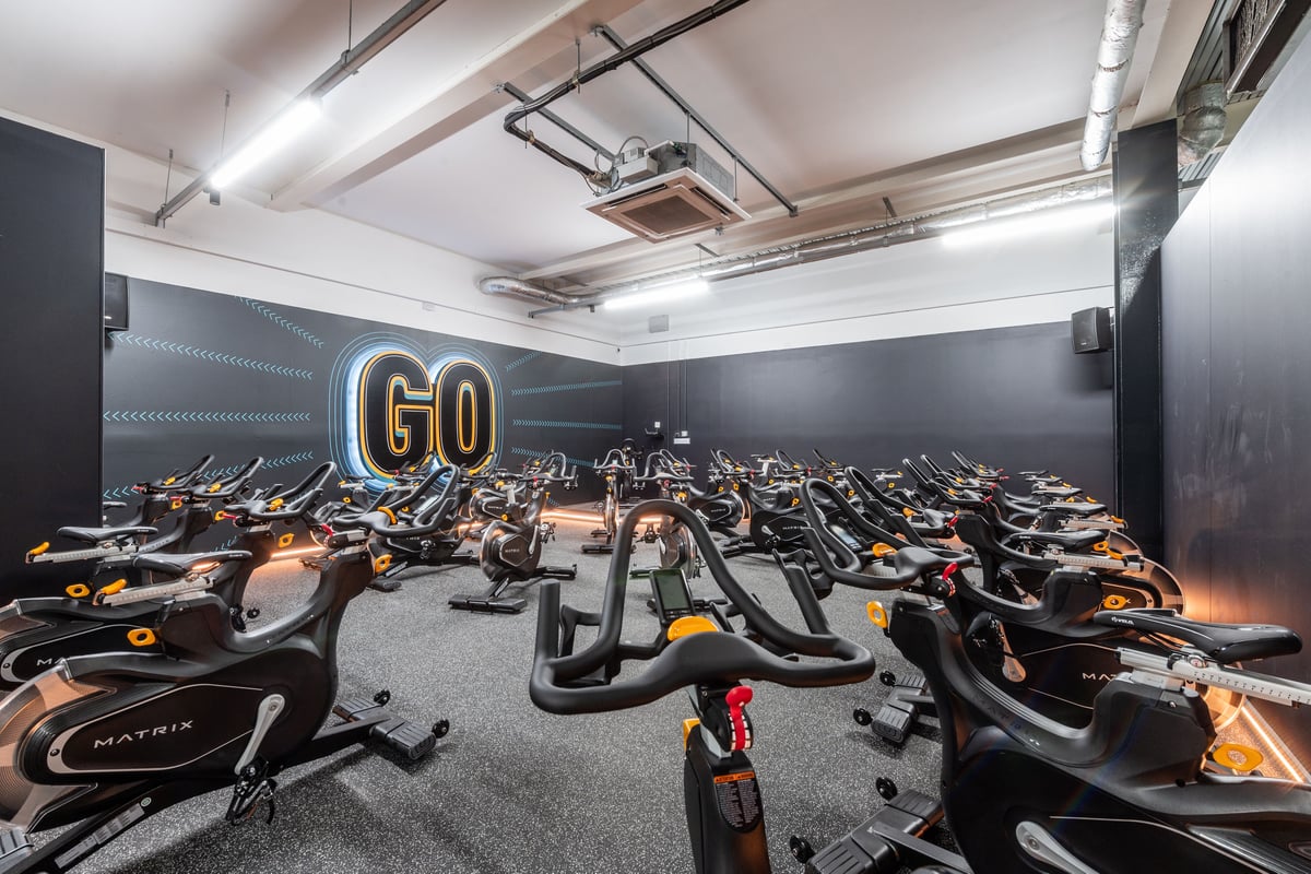 PureGym Harrogate: Rows of stationary exercise bikes in a dimly lit studio with "GO" illuminated on the wall.