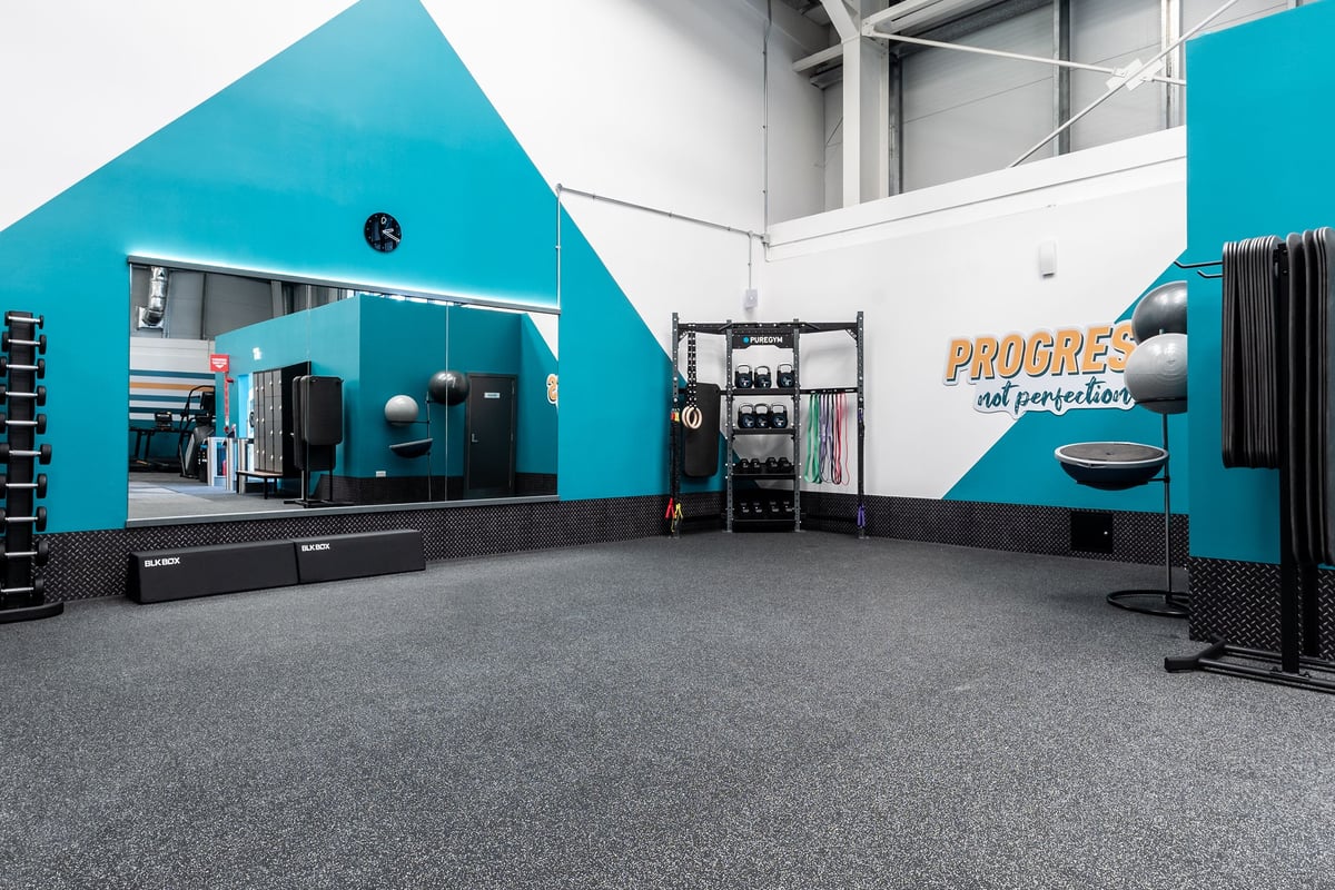 PureGym Kettering: Fitness studio with turquoise walls, weight racks, resistance machines, rubberized flooring.