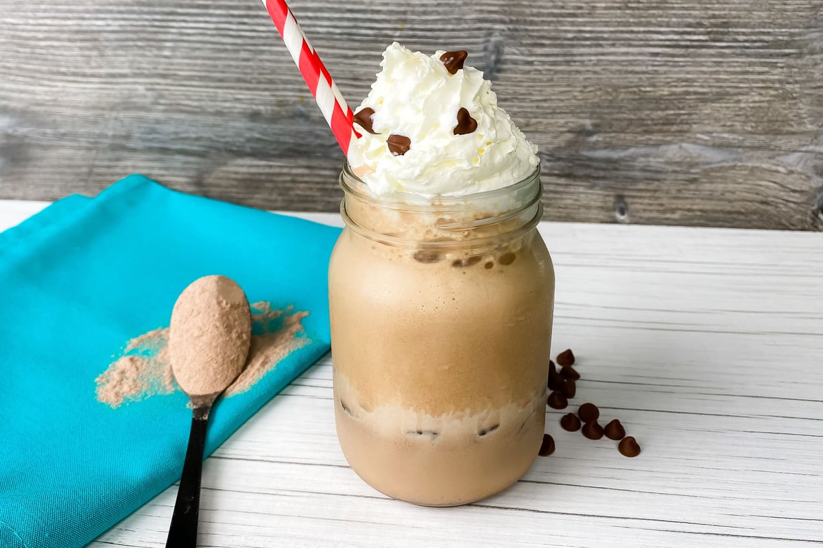 Iced coffee drink topped with whipped cream in a glass jar with protein powder nearby