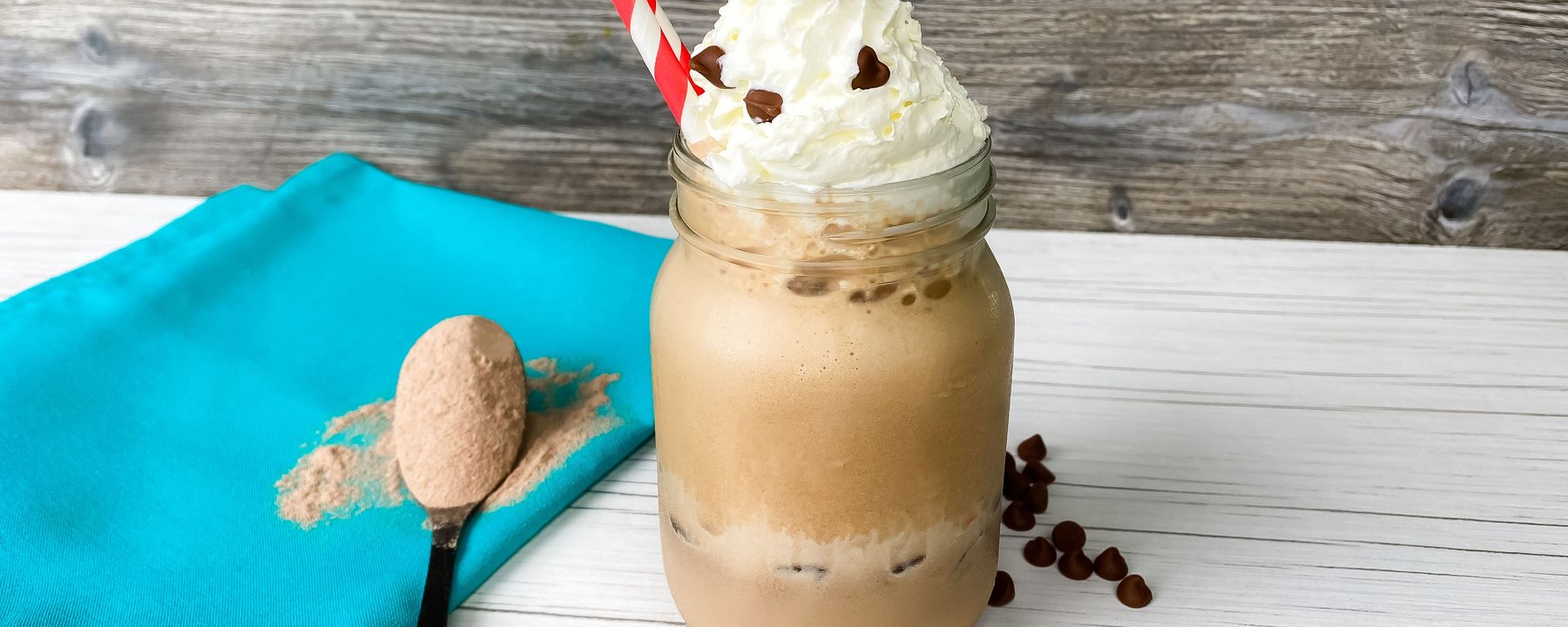 Iced coffee drink topped with whipped cream in a glass jar with protein powder nearby