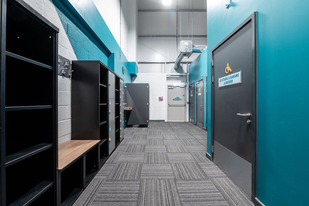 PureGym Alton: Locker room with black cabinets, benches, and contrasting teal decor.