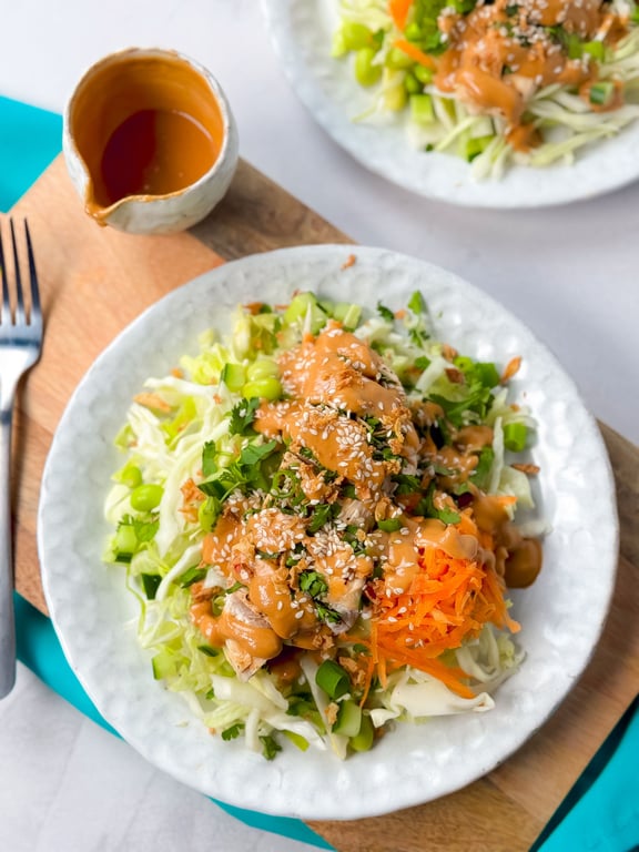 Salad with shredded carrot, cabbage, edamame, chicken, sesame seeds, and dressing on white