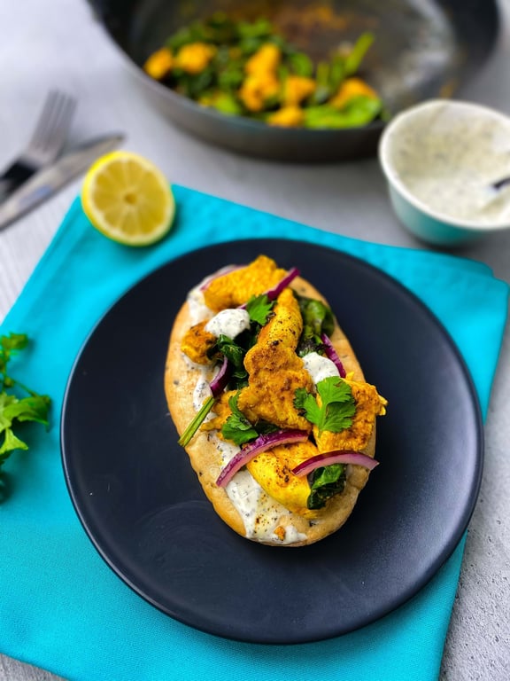 Flatbread topped with grilled chicken, sauce, red onions, and fresh herbs on a black plate