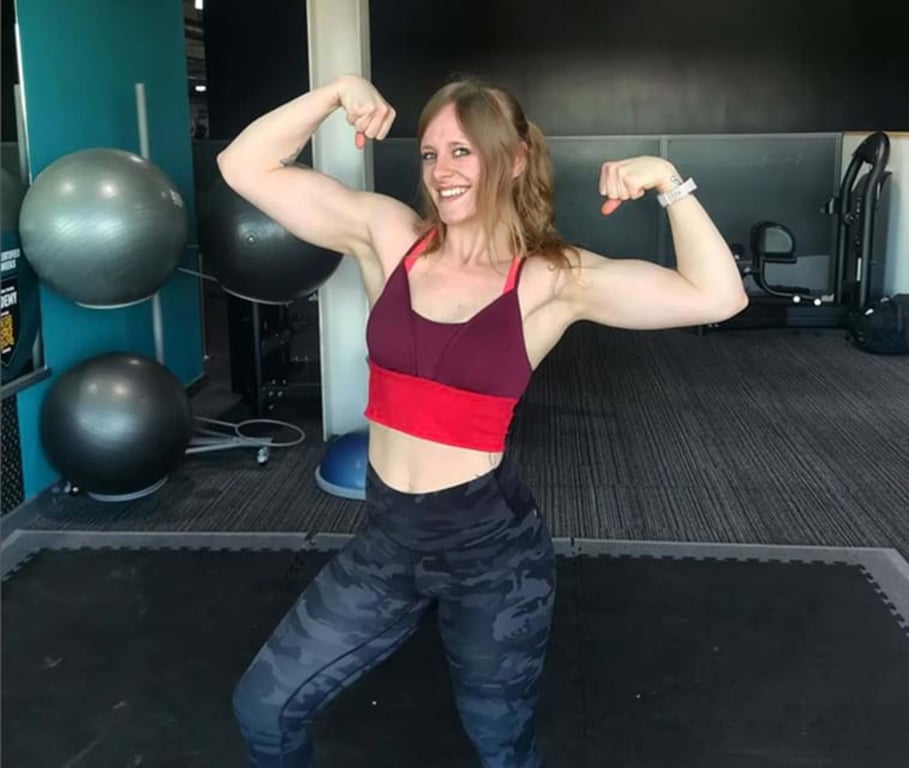 Woman in gym wear flexing biceps with exercise balls and equipment in background