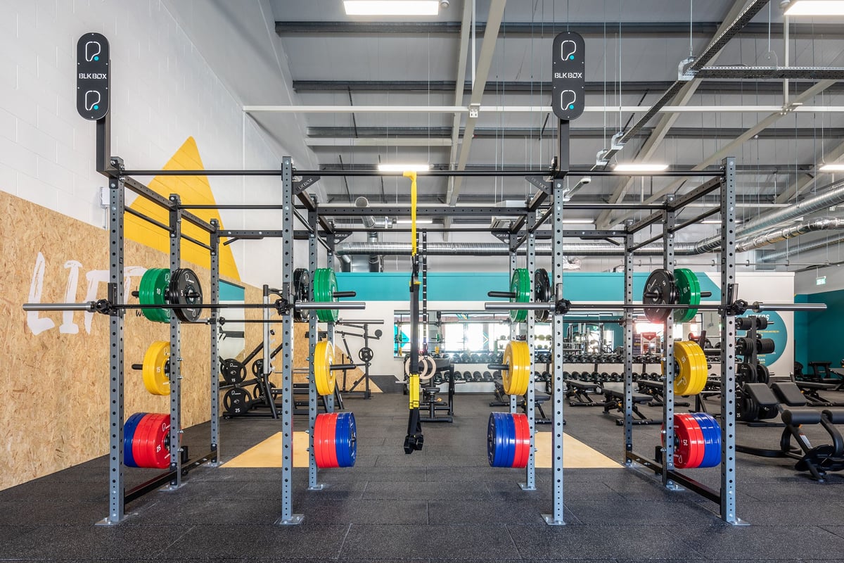 PureGym Ebbw Vale: Squat racks, weight plates in vibrant colours, rubberized flooring in a spacious gym setting.