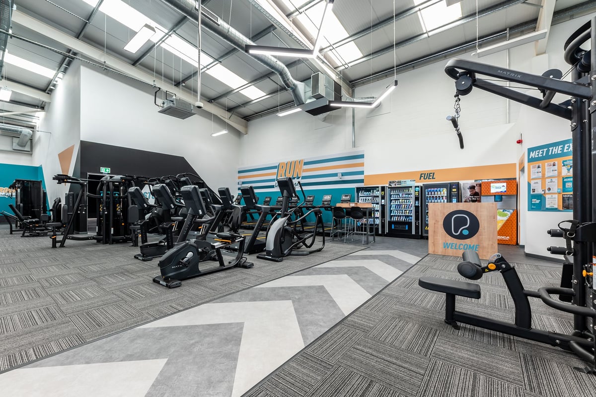 PureGym Dumfries: Rows of ellipticals, stationary bikes, and strength training equipment in a gym setting with bright colors.