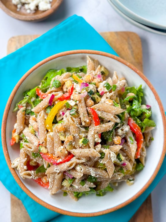 Bowl of whole wheat penne pasta salad with chickpeas, red and yellow peppers, and herbs.