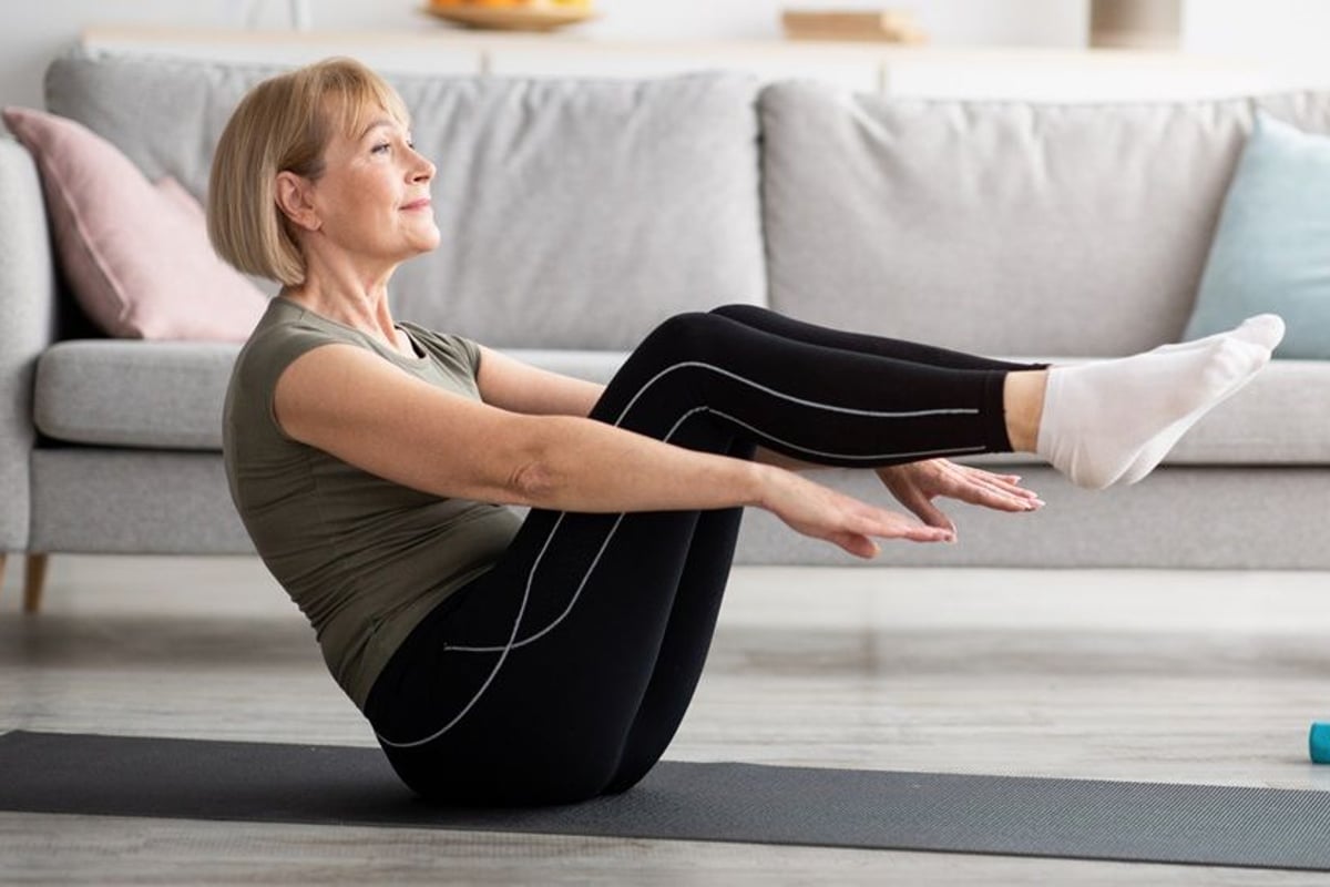 Woman in olive top performing boat pose core exercise on mat in living room