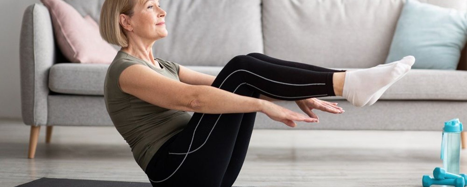 Woman in olive top performing boat pose core exercise on mat in living room