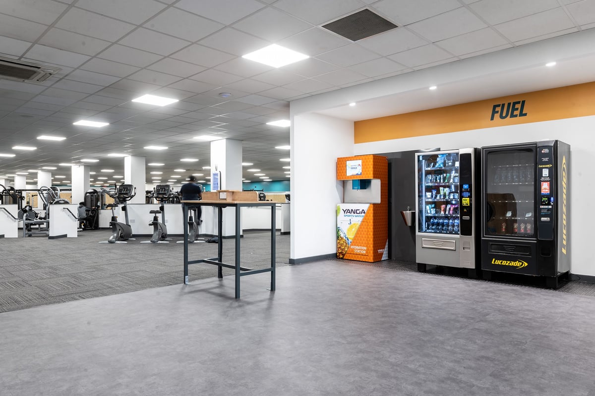 PureGym Birmingham Beaufort Park: Rows of cardio machines, vending machines, and seating area in a bright gym space.