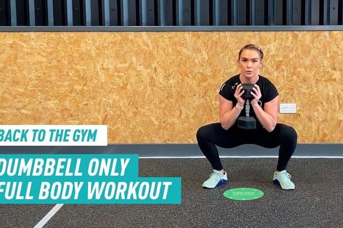 Woman in black workout clothes holding dumbbell in a squat position on gym floor