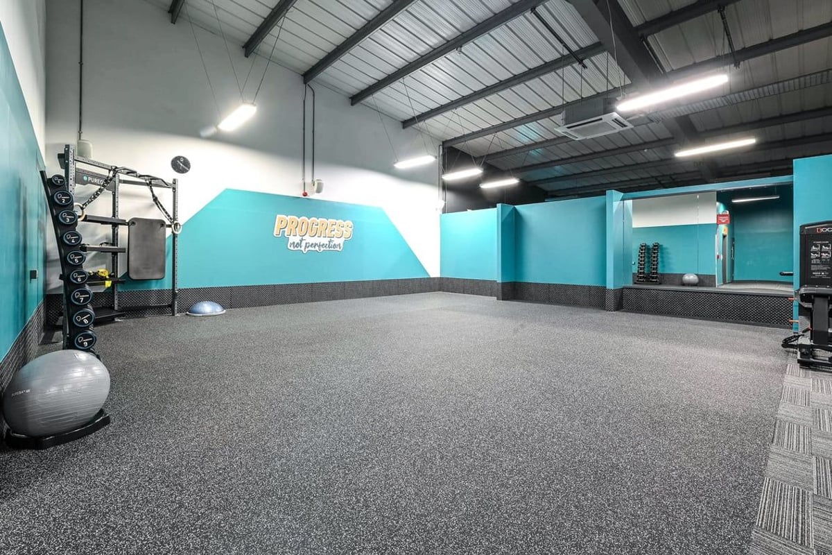 PureGym Canterbury Sturry Road: Fitness studio with rubberized flooring, weight racks, medicine balls, and teal accent walls.