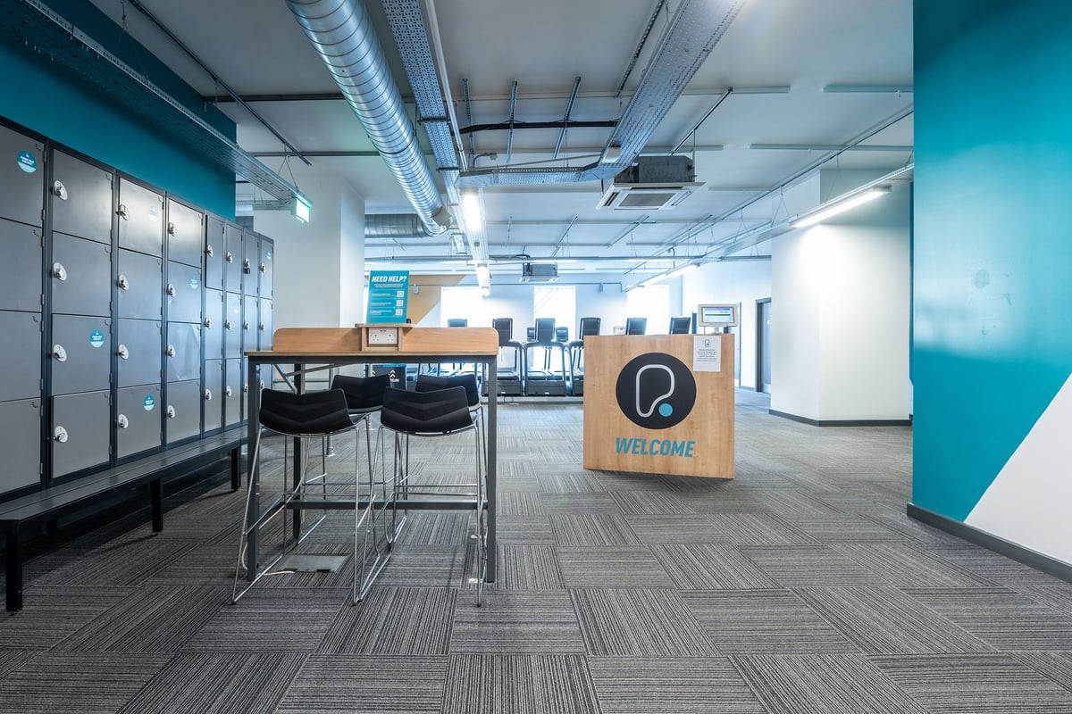 PureGym Stevenage: Lockers, table with chairs, and a welcome sign in a modern office space.