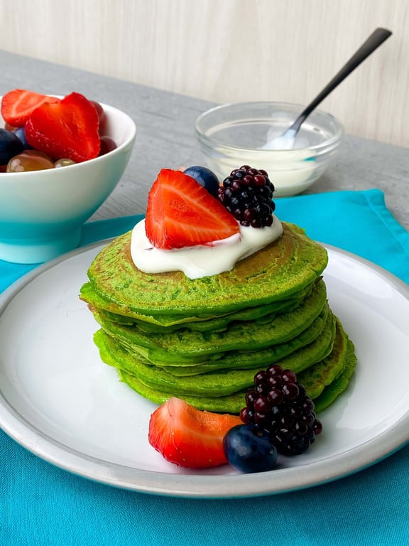 Stack of green pancakes topped with cream, strawberries, blackberries, and blueberries on