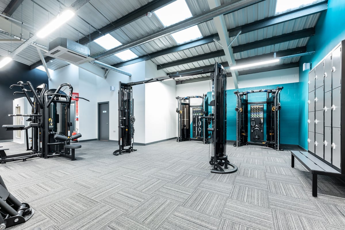 PureGym Boston: Strength training area with cable machines, squat racks, benches, and rubberized flooring.