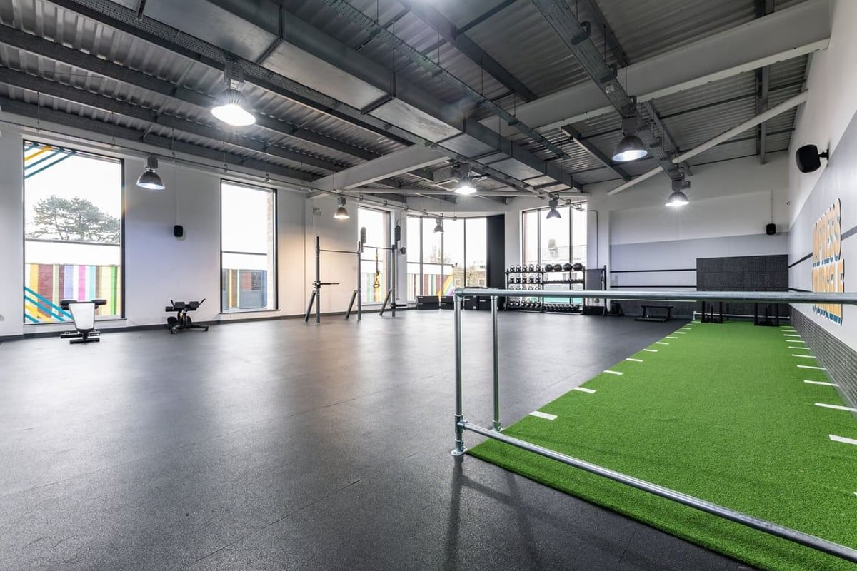 PureGym Nottingham Beeston: Green turf section, free weights, mirror-walled studio with industrial ceiling beams.