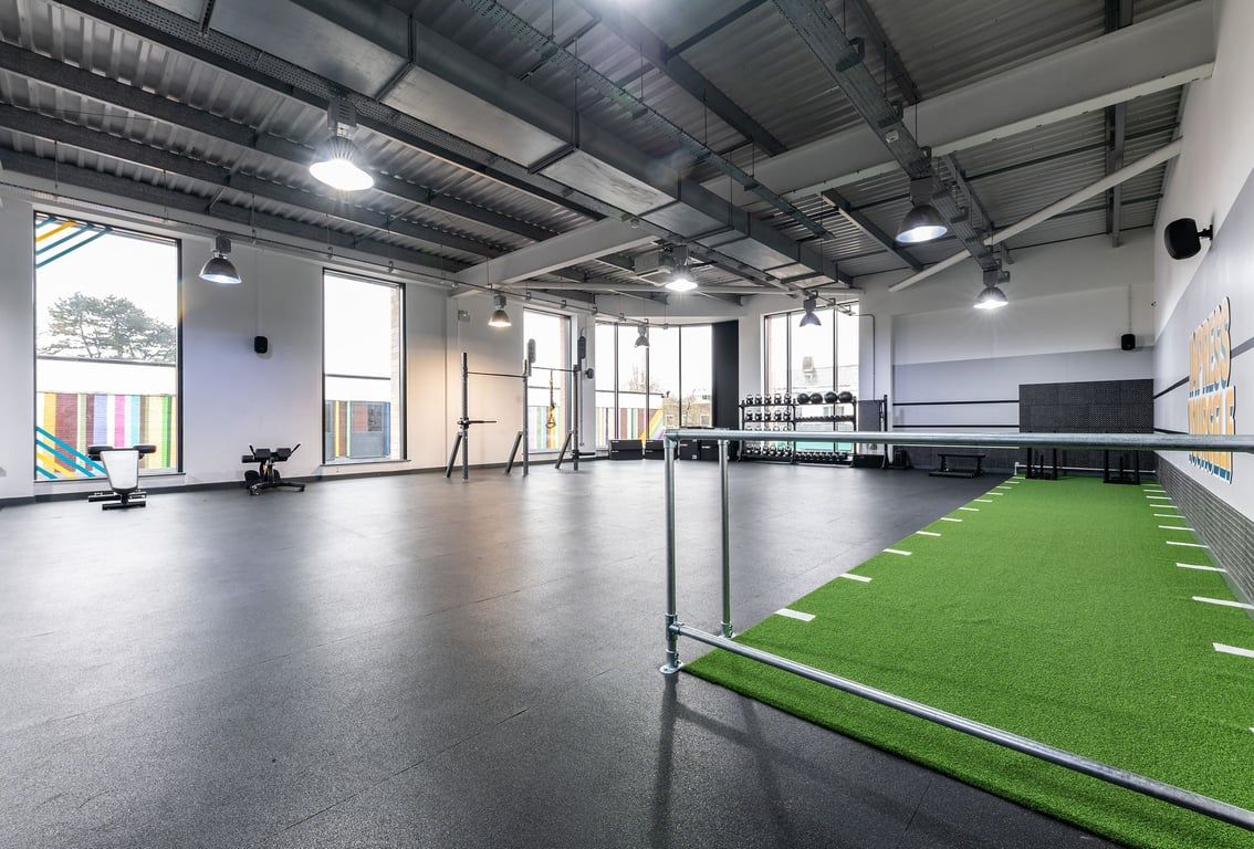 PureGym Nottingham Beeston: Green turf section, free weights, mirror-walled studio with industrial ceiling beams.