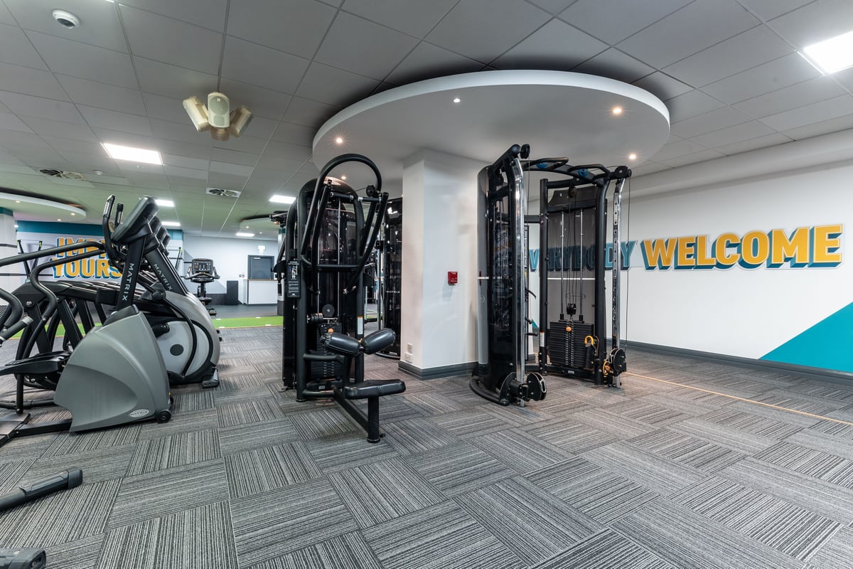 PureGym London Edgware: Weight machines, resistance equipment, welcome sign, and patterned flooring inside a gym space.