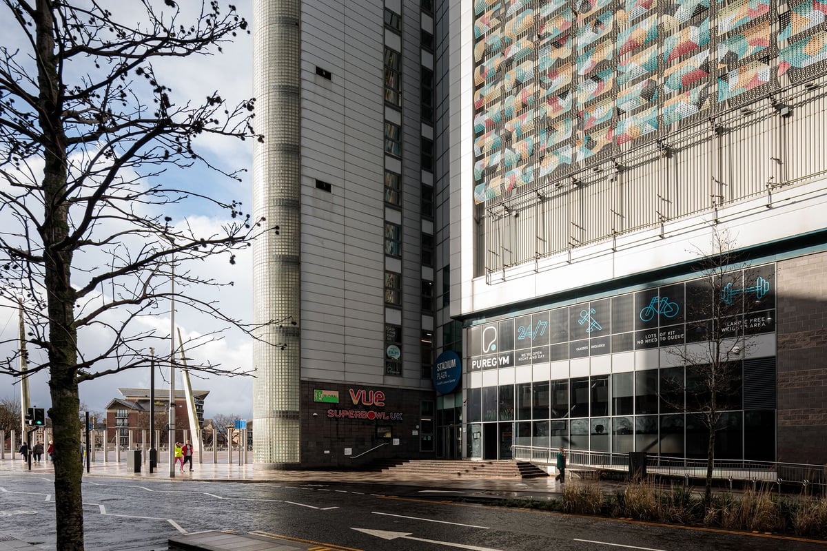 PureGym Cardiff Central: Exterior city street with modern high-rise buildings and public transport signage.