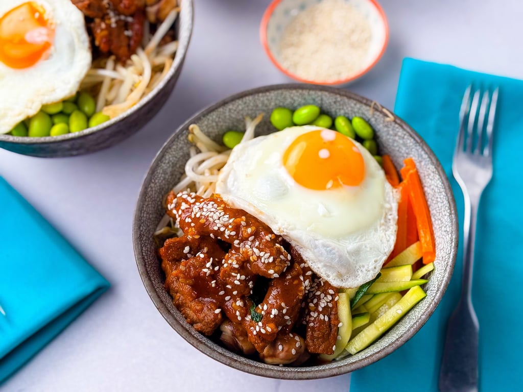 Bowl with fried egg, sesame chicken, edamame, carrots, and zucchini strips with fork