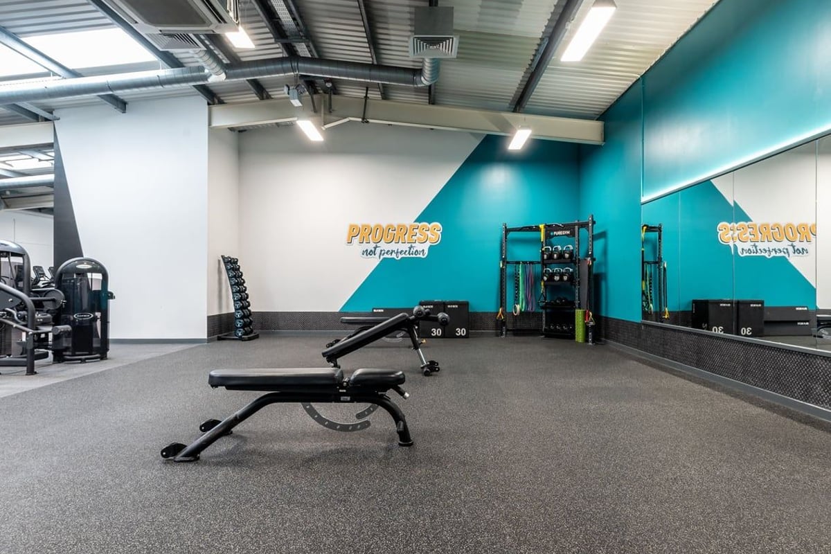 PureGym Gloucester Retail Park: Weight benches, resistance machines, rubberized floors in fitness studio with teal accents.