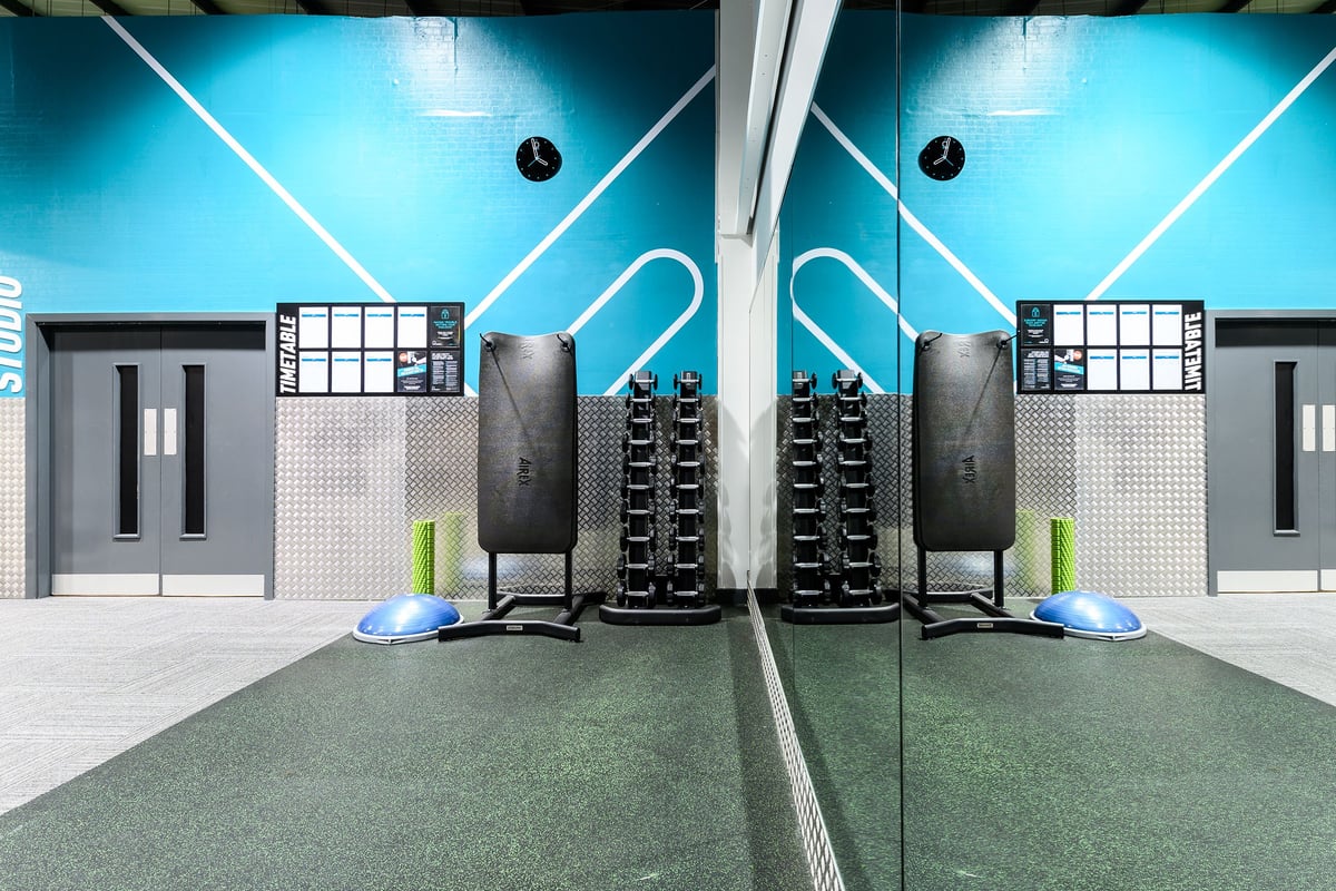 PureGym Bromborough: Squat racks, weight plates, rubberized turf flooring, and neon lighting in a modern gym setting.