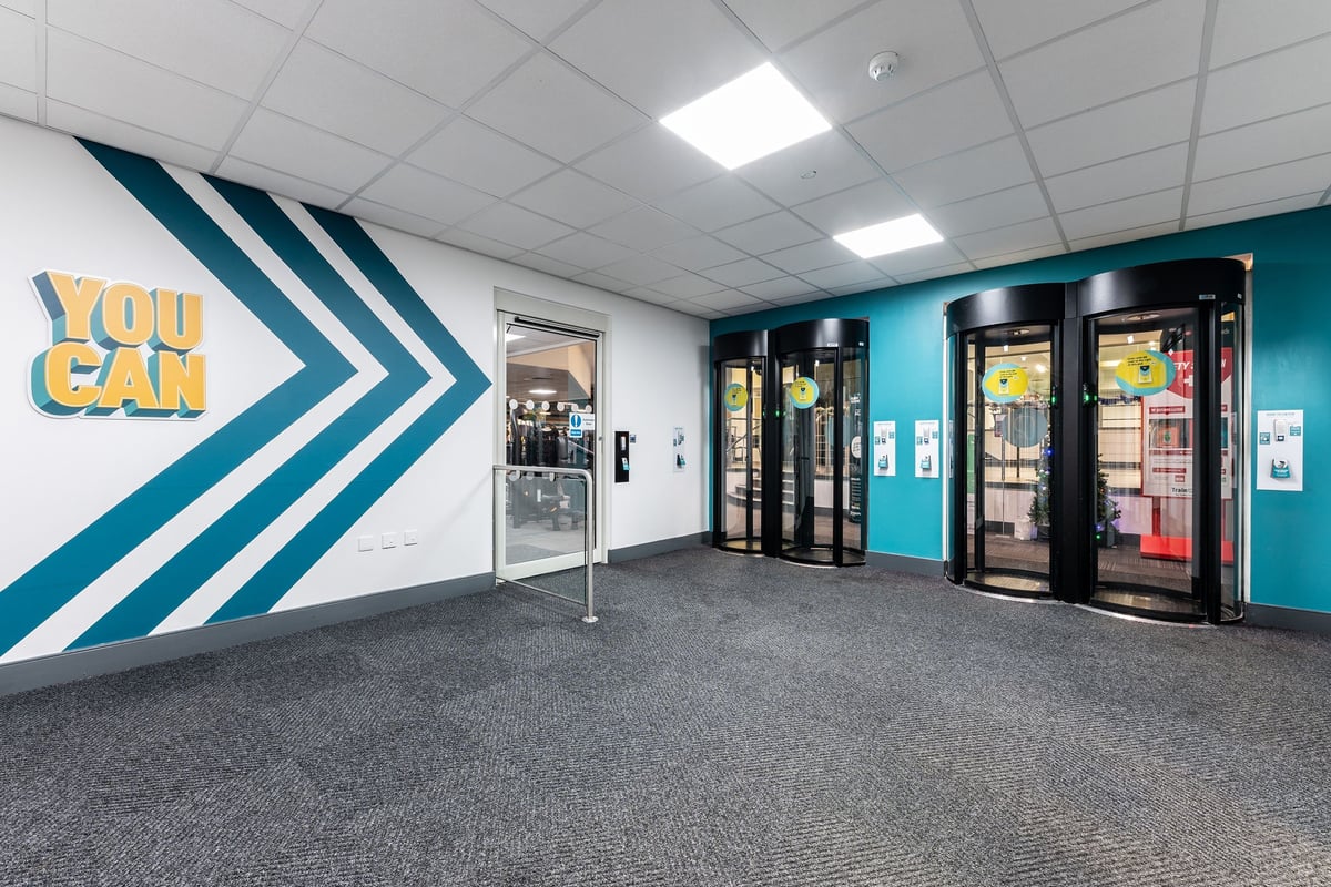 PureGym Cambridge Leisure Park: Entrance area with vending machines, turnstiles, and motivational wall graphics.