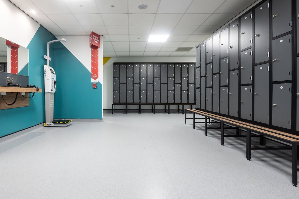 PureGym Edinburgh Exchange Crescent: Grey lockers, benches along centre, fitness posters on teal accent wall.
