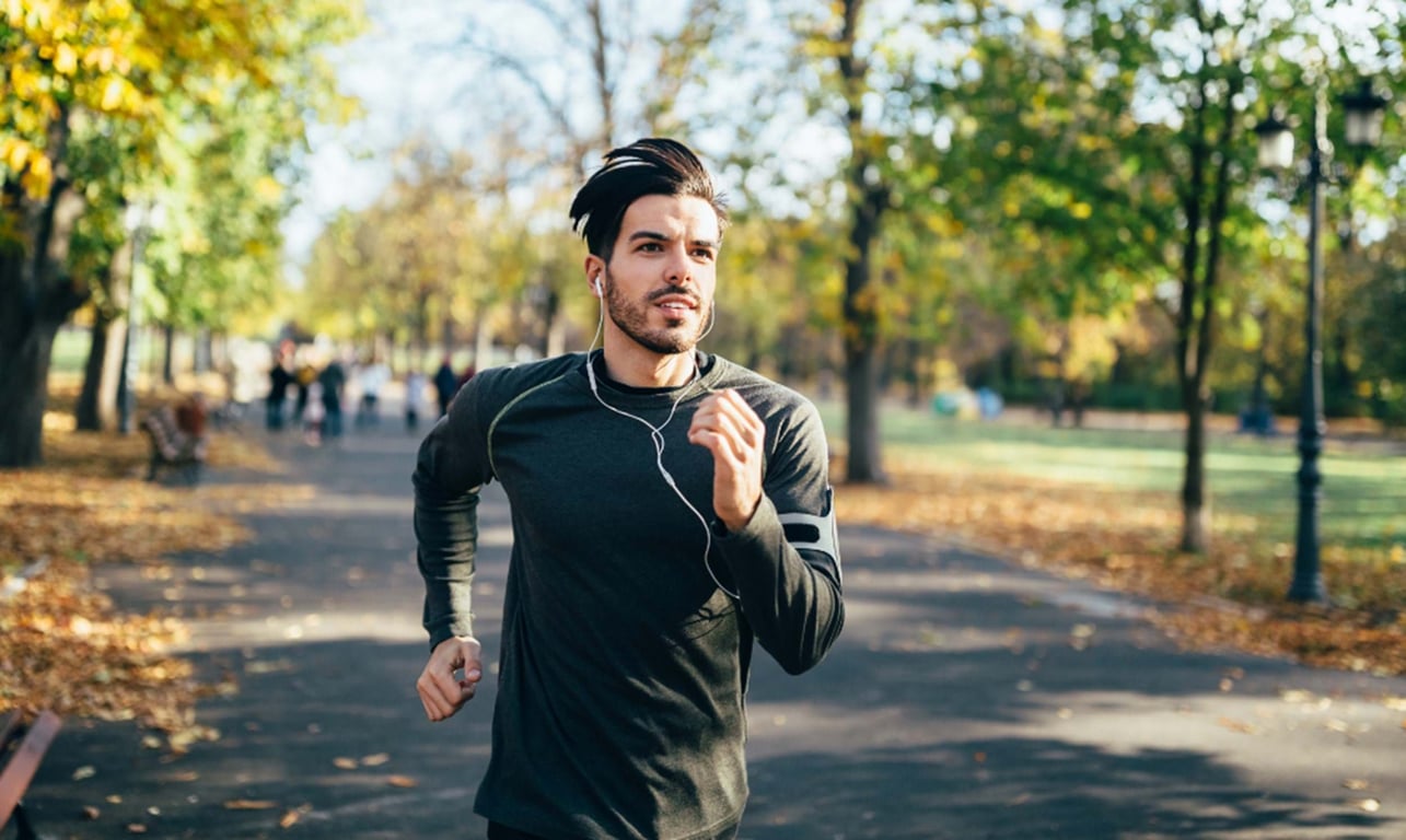 Man jogging in autumn park wearing earphones and a black long-sleeve shirt