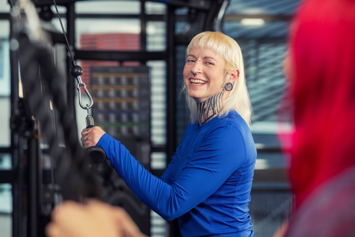Frau in blauem Oberteil lächelnd mit Kabel in modernem Fitnessstudio