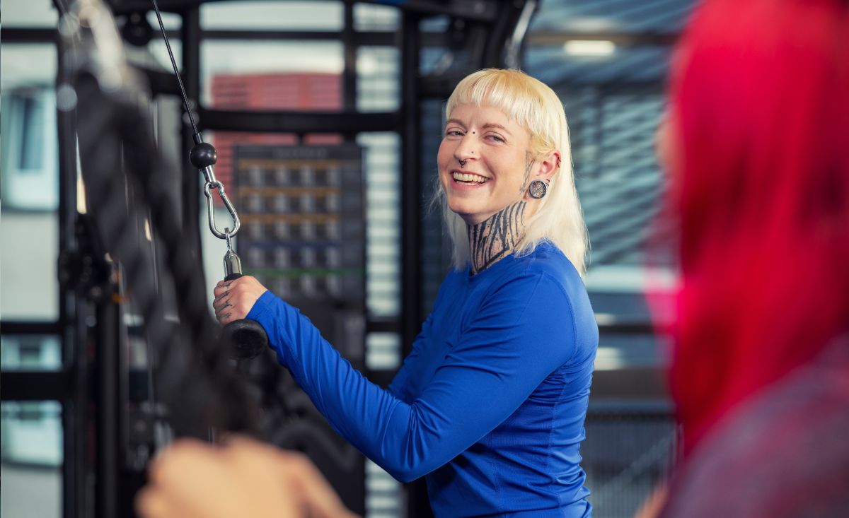 Frau in blauem Oberteil lächelnd mit Kabel in modernem Fitnessstudio