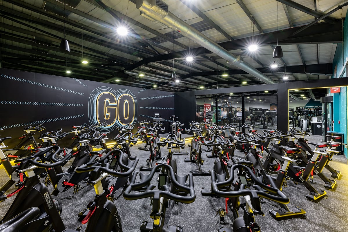 PureGym Lincoln St Marks Centre: Rows of stationary bikes clustered in a dimly lit space with ceiling lamps and "GO" signage.