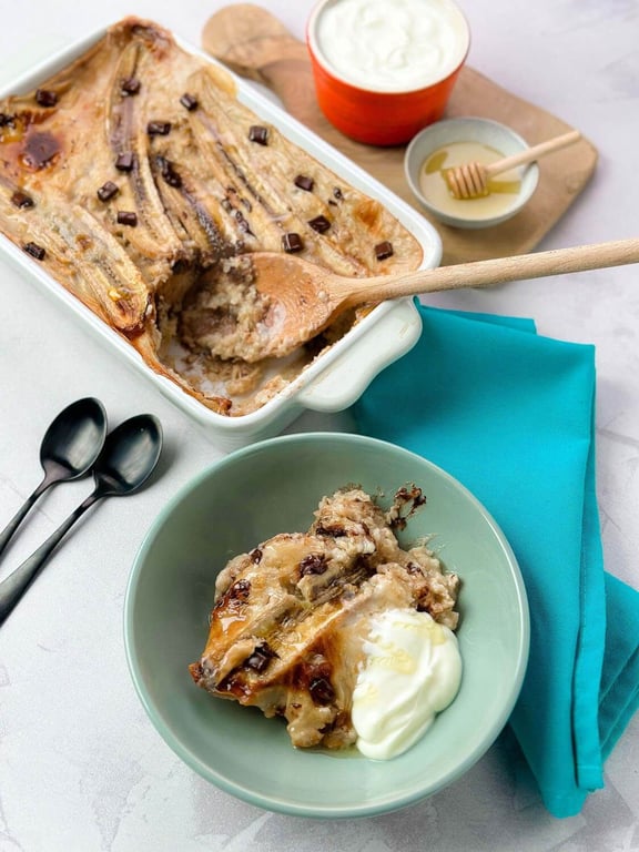 Baked banana dessert with chocolate chips served with cream and honey on a teal napkin