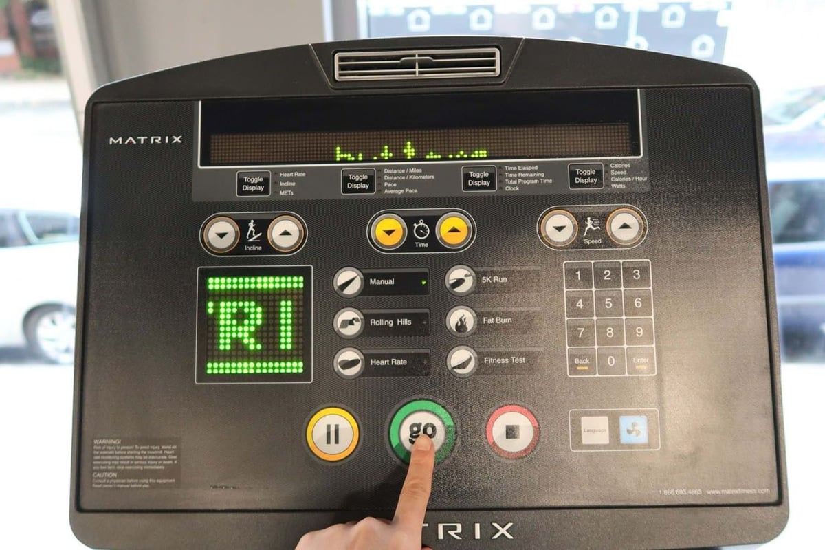 Hand pressing green go button on treadmill control panel with digital display and buttons