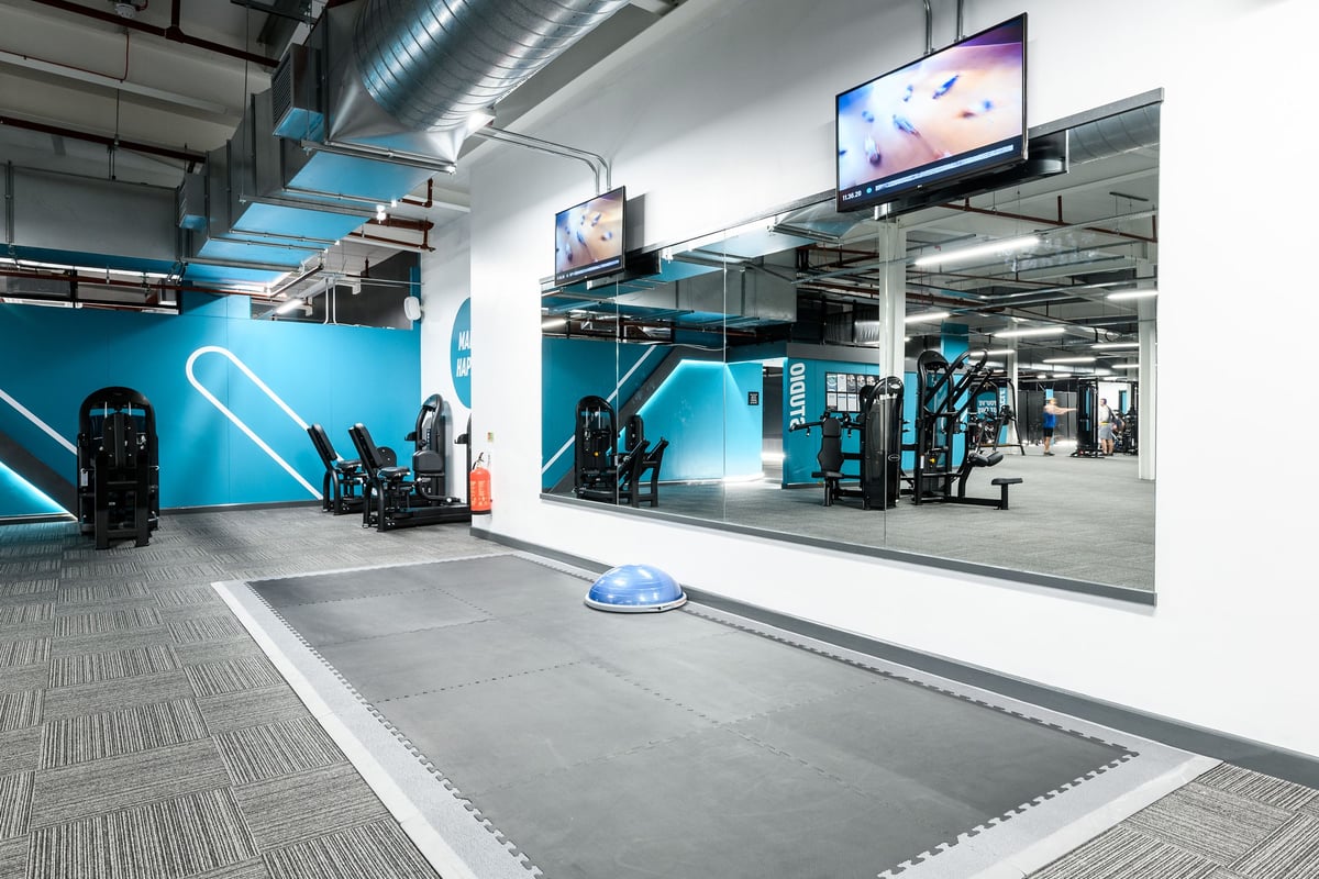 PureGym Cambridge Grafton Centre: Gym studio with teal accents, weight machines, mirrored walls, and rubberized flooring.