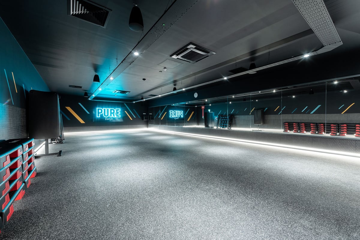 PureGym Tyldesley: Teal-lit studio with rubberized floor, red benches, no fitness equipment visible.