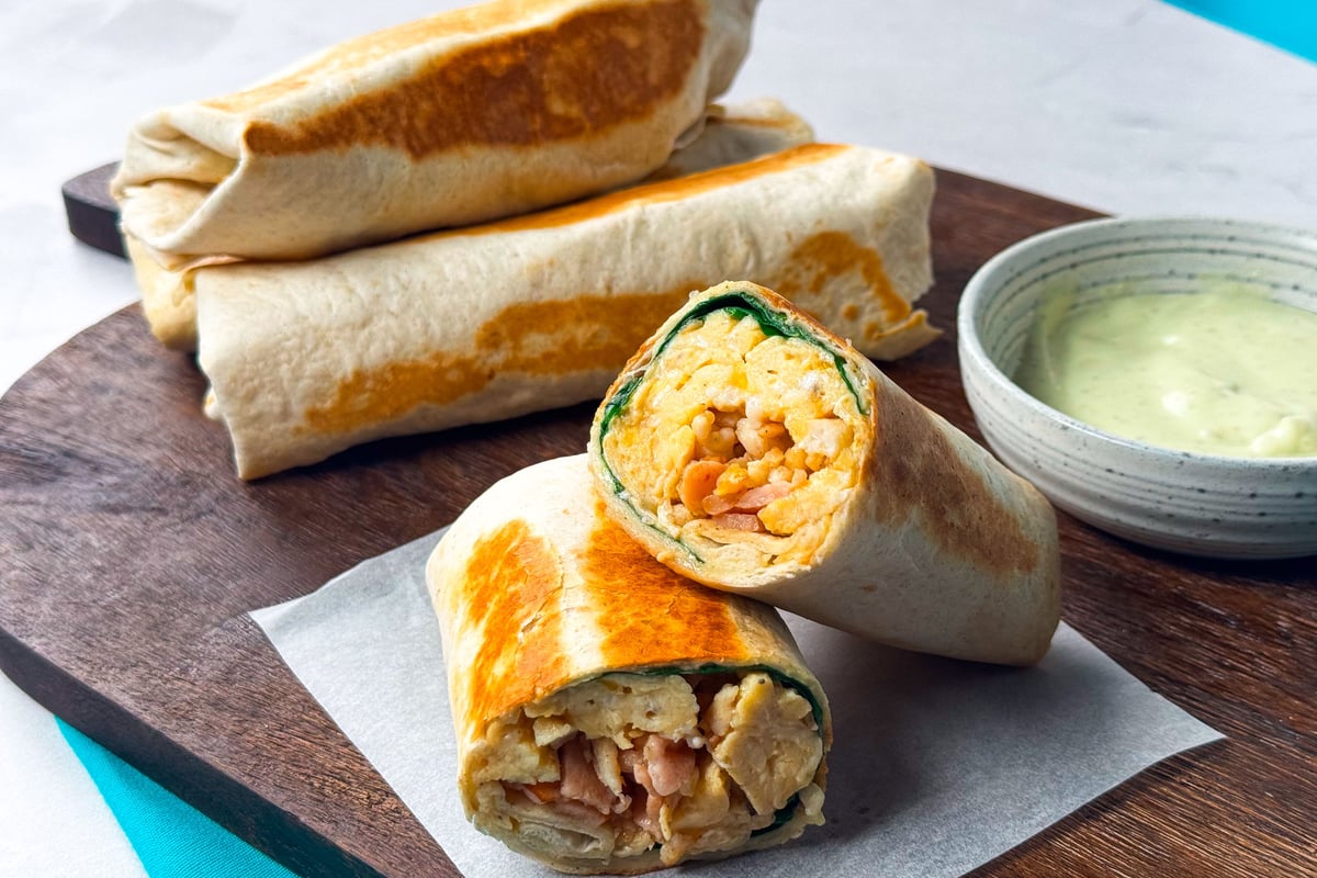 Grilled wraps filled with scrambled eggs, bacon, and spinach served with sauce.